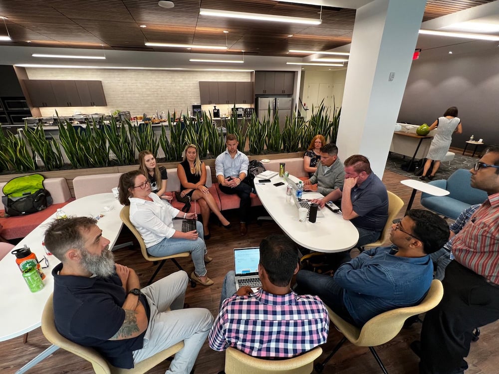 Group of professionals engaged in a roundtable discussion in a modern office break room.